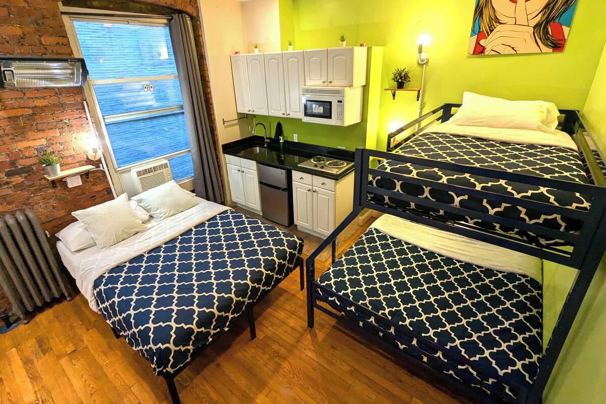 Ein Zimmer mit zwei Etagenbetten, einer Küchenzeile, einer Ziegelwand und einem Fenster mit Jalousien.