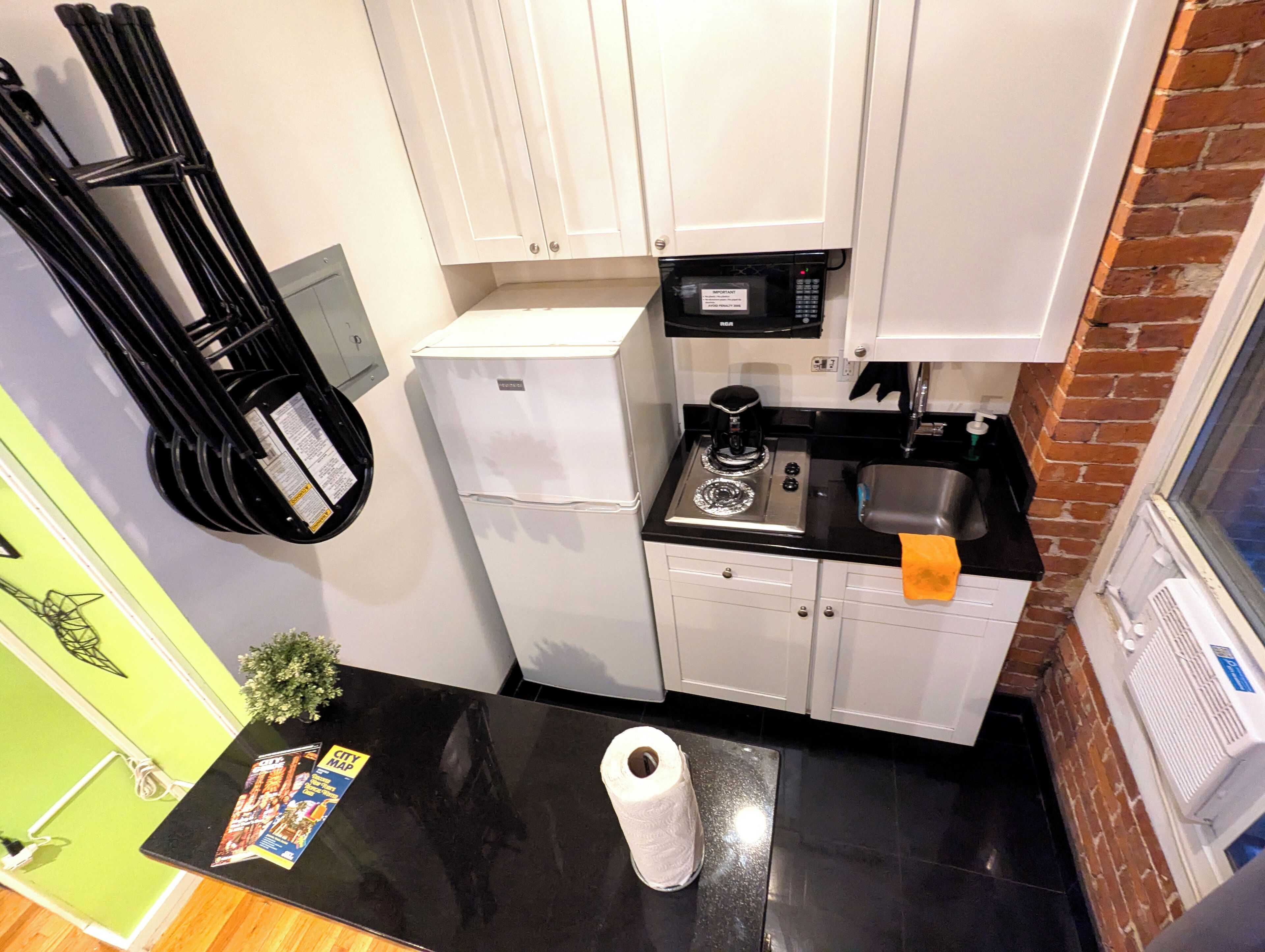 A compact kitchen with white cabinets, a black countertop, a refrigerator, a microwave, a stove, and a sink.