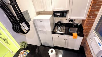 A compact kitchen with white cabinets, a black countertop, a refrigerator, a microwave, a stove, and a sink.
