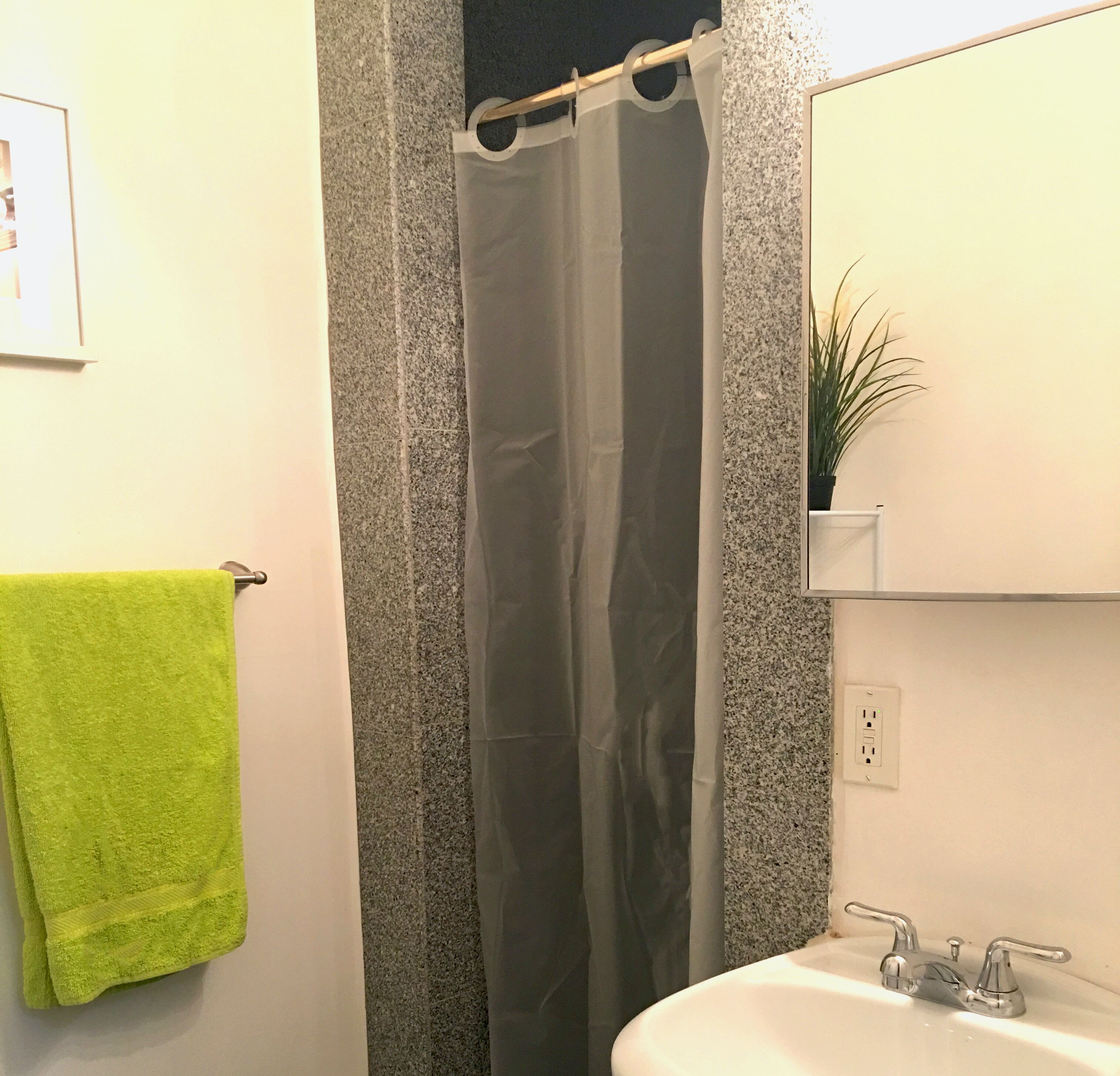Une salle de bain avec un rideau de douche, une serviette verte, un lavabo et un miroir.