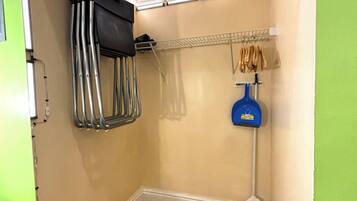 Canto de um quarto com soalho de madeira, uma estante de metal, um balde azul para limpeza e um extintor de incêndio vermelho.