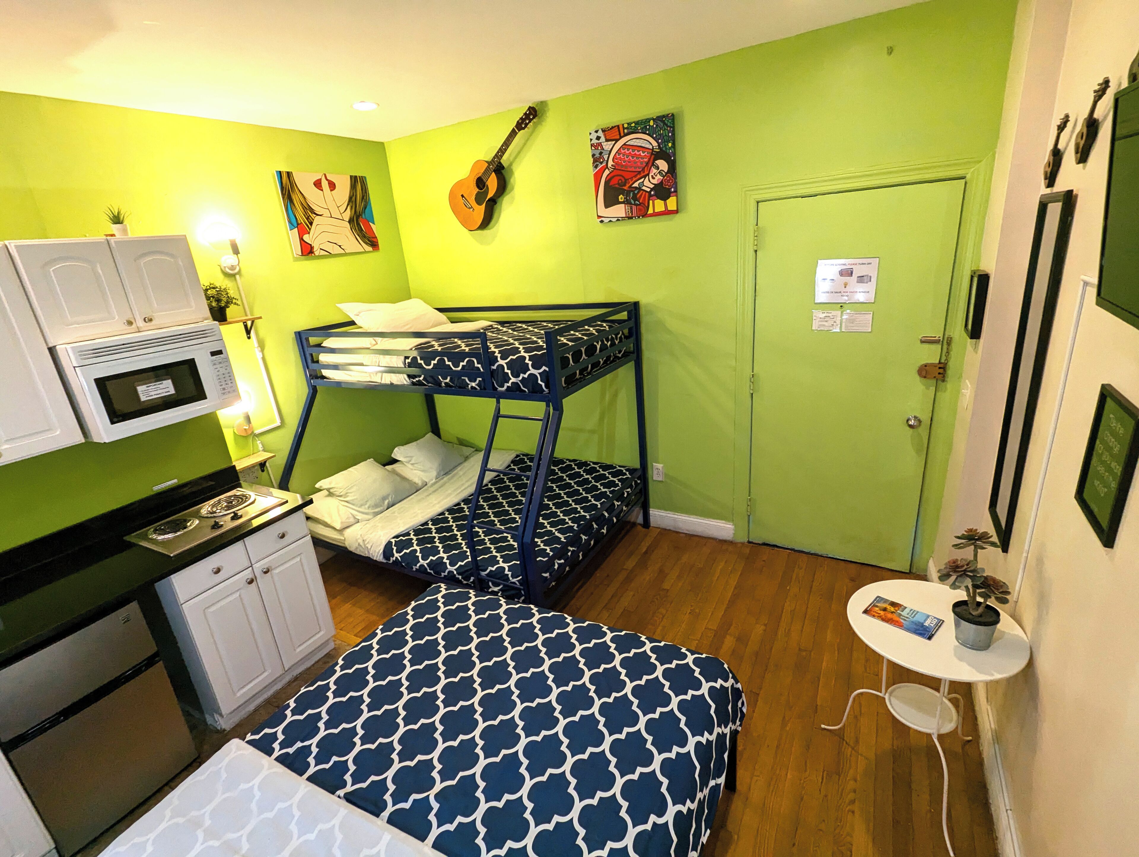 A compact room with a bunk bed, kitchenette, and a small table with a plant.