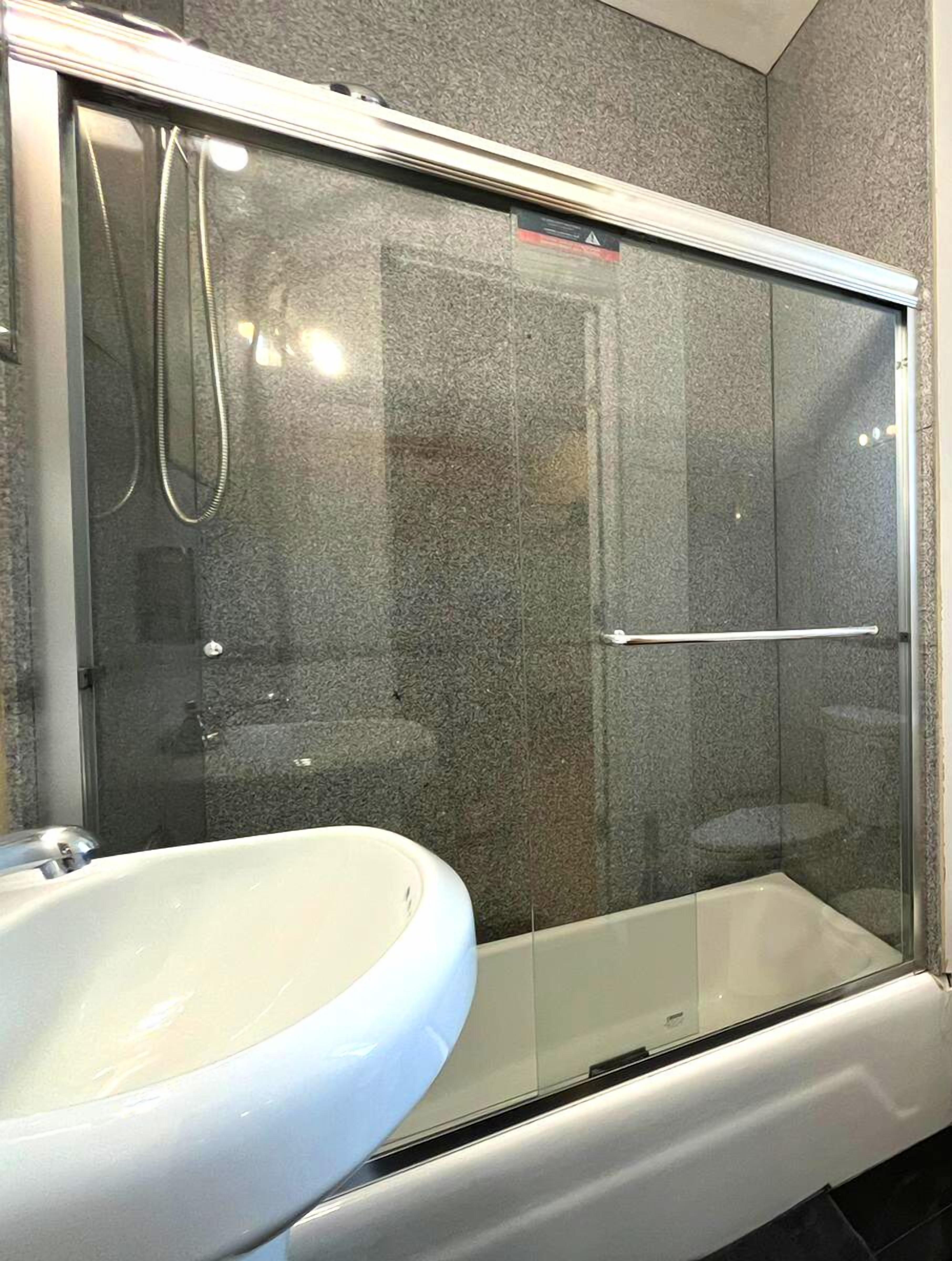 A bathroom with a glass-enclosed shower, a white sink, and a tiled wall.