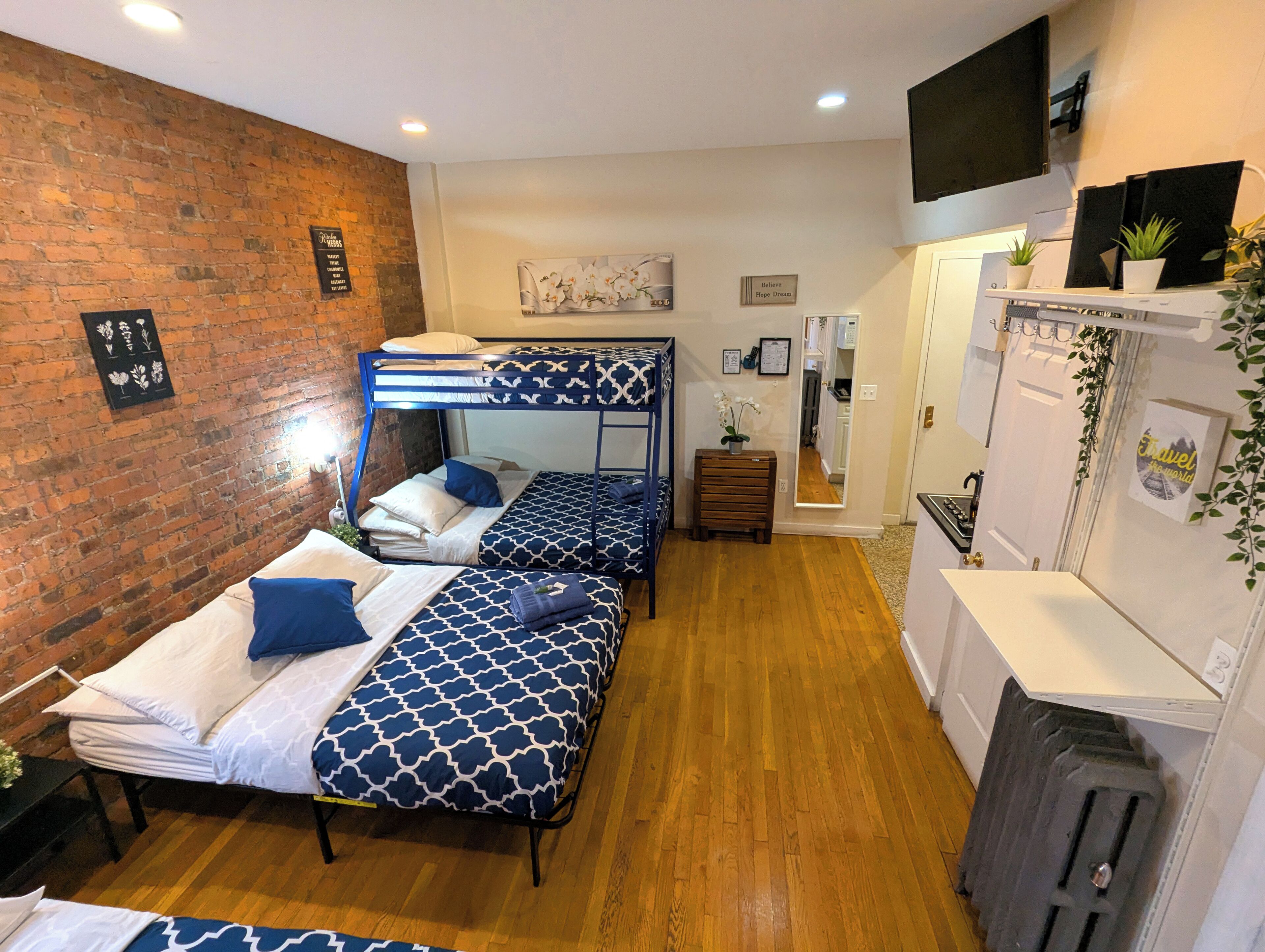 A dormitory room with bunk beds, a brick wall, a wooden floor, a TV, and a small plant.