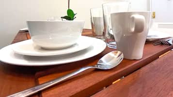 Una mesa de comedor con platos blancos, un bol, una taza y una cuchara.