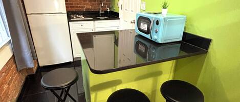 A compact kitchen with white cabinets, a refrigerator, a microwave, and a small island with stools.