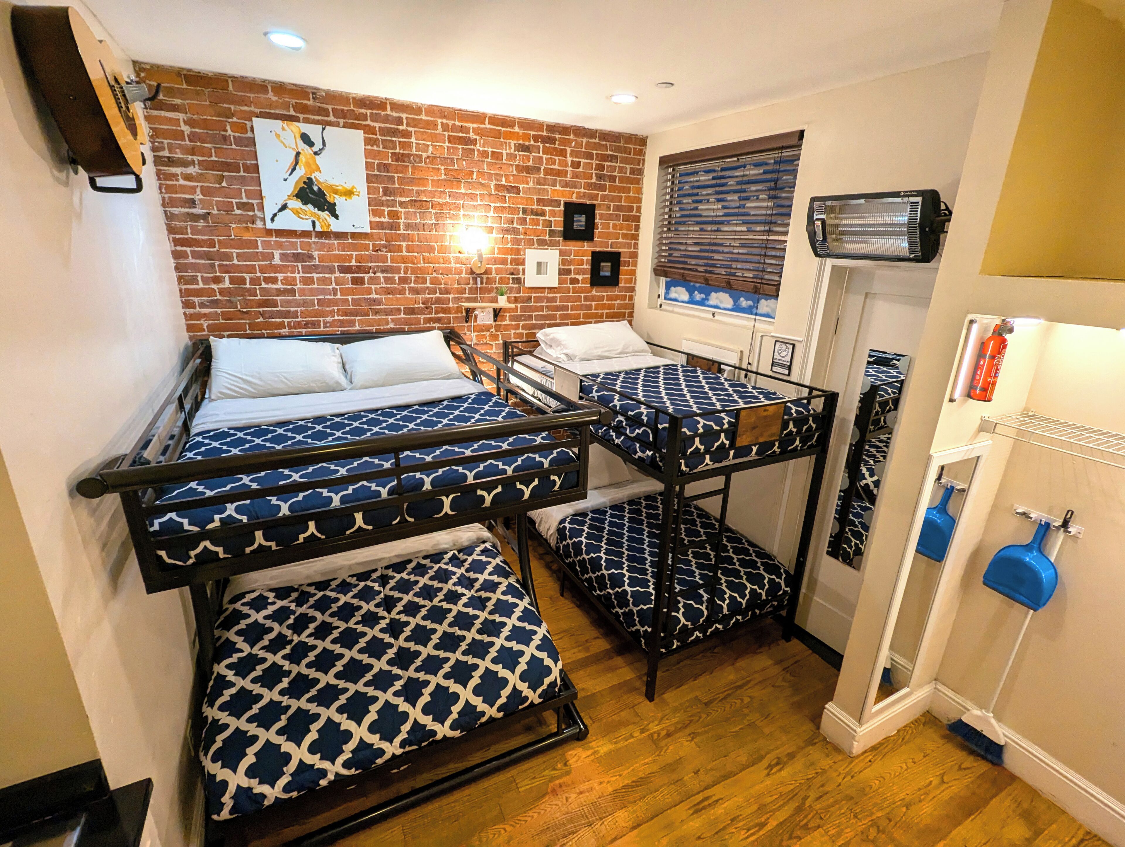Een kleine kamer met stapelbedden, een bakstenen muur, een gitaar en een schilderij.