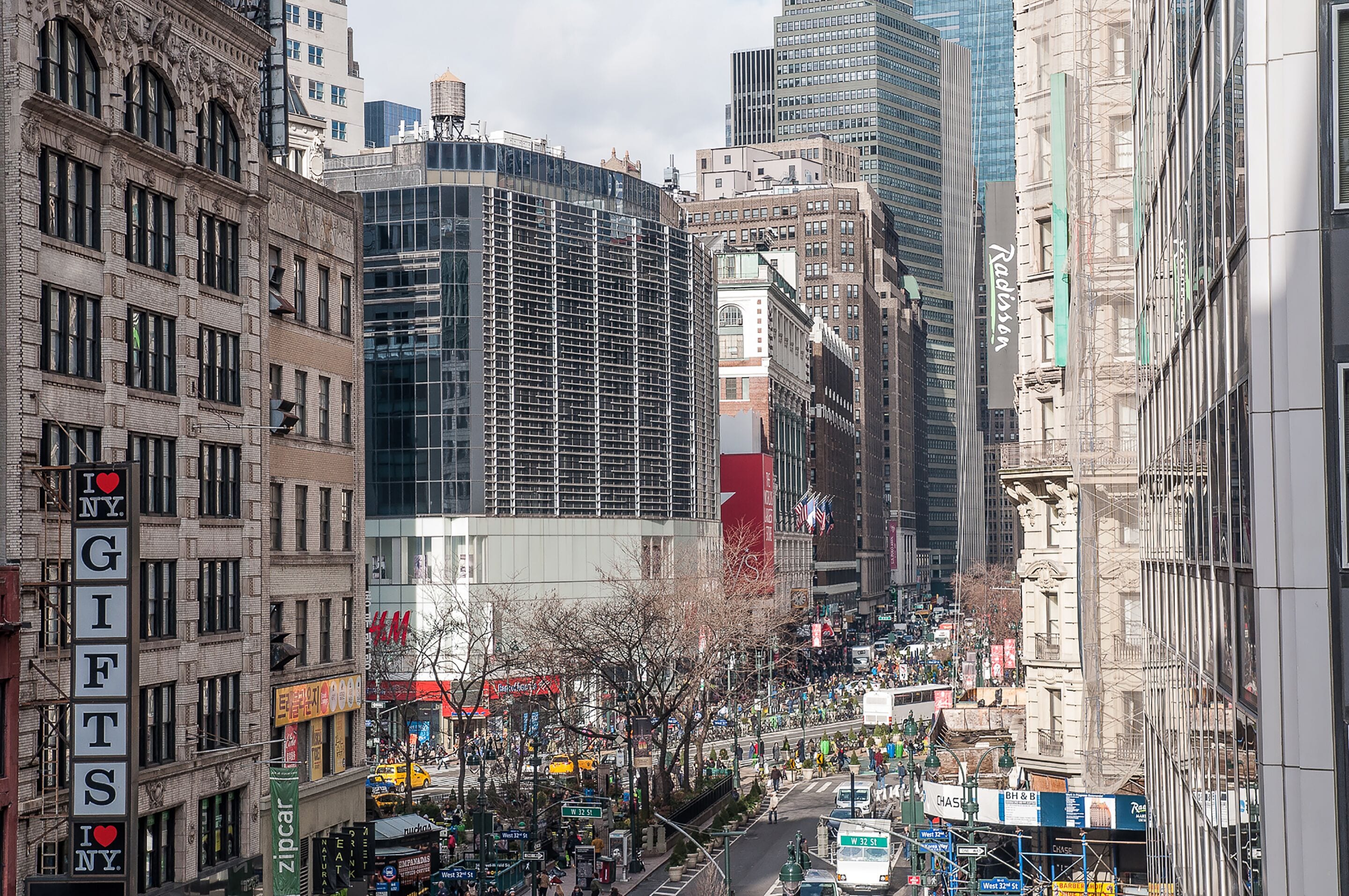 A busy urban street with historic buildings, a modern glass structure, and various commercial signs.