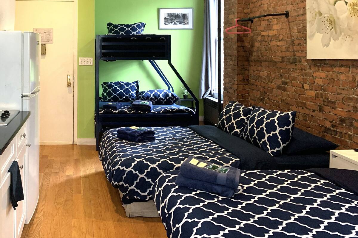 Eine kleine Küche mit Spüle, Herd und weißen Schränken. Ein Stockbett mit gemusterten Betttextilien steht an einer grünen Wand.