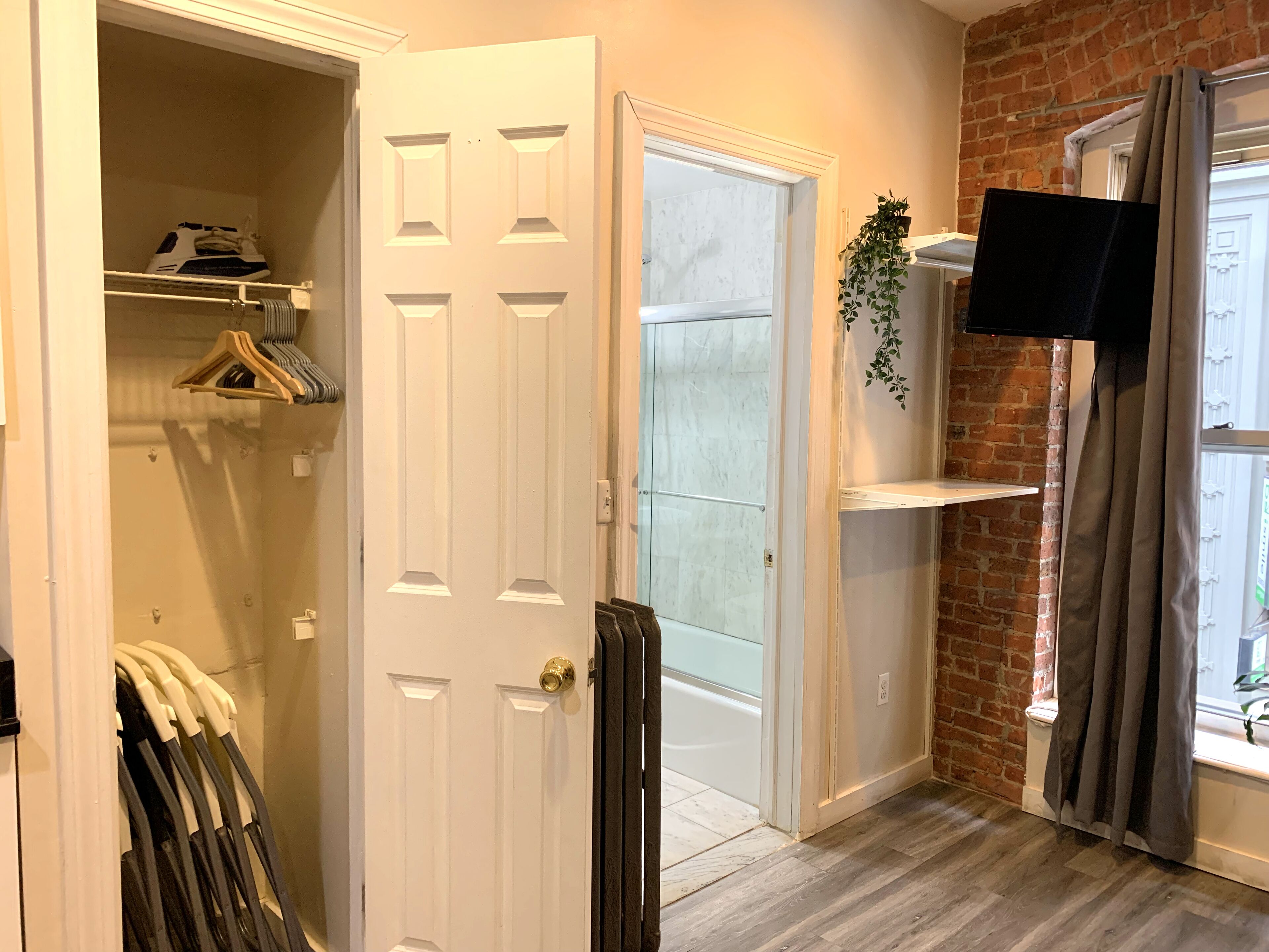 A room with a white door, a brick wall, a mounted TV, and a window with curtains.