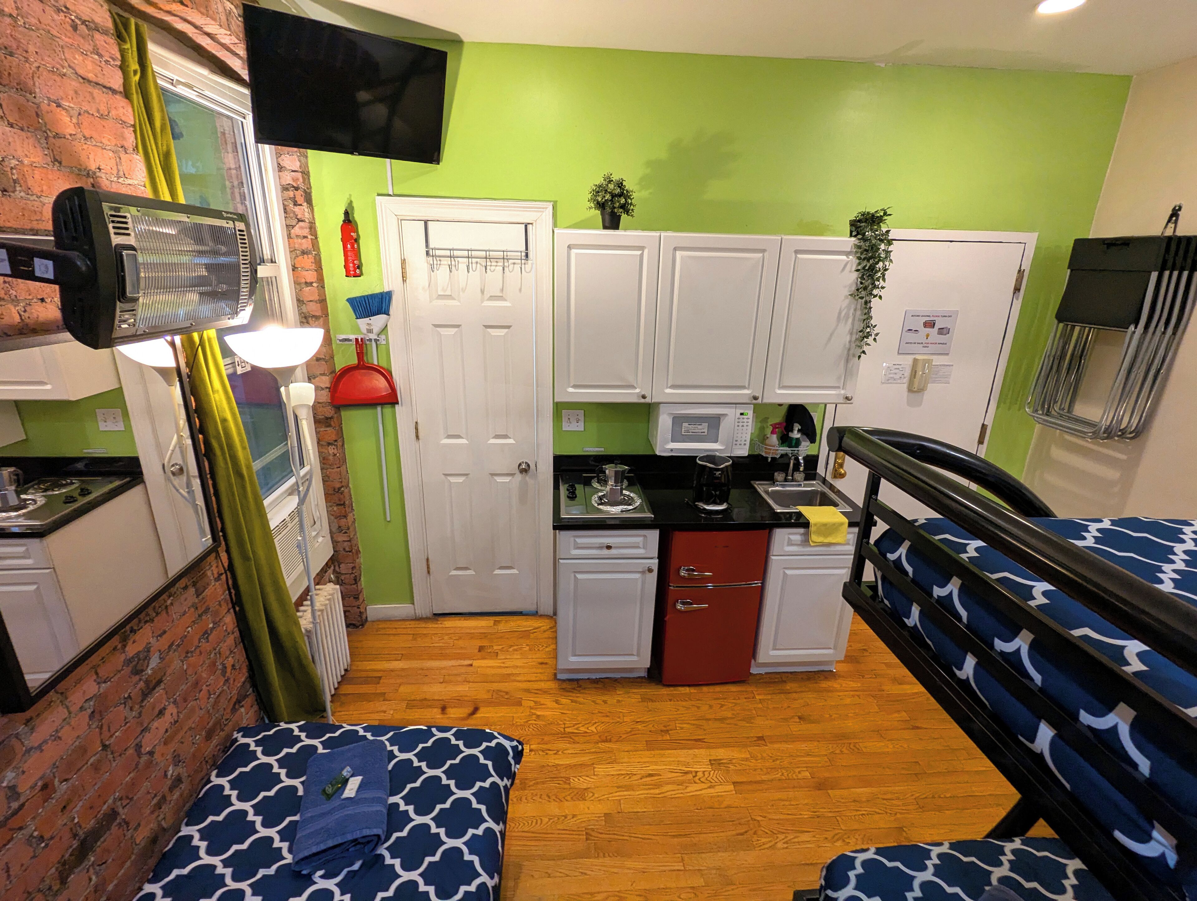 Une pièce compacte dotée d’une kitchenette, d’un lit avec une literie à motifs, d’un téléviseur fixé au mur et d’un mur vert.