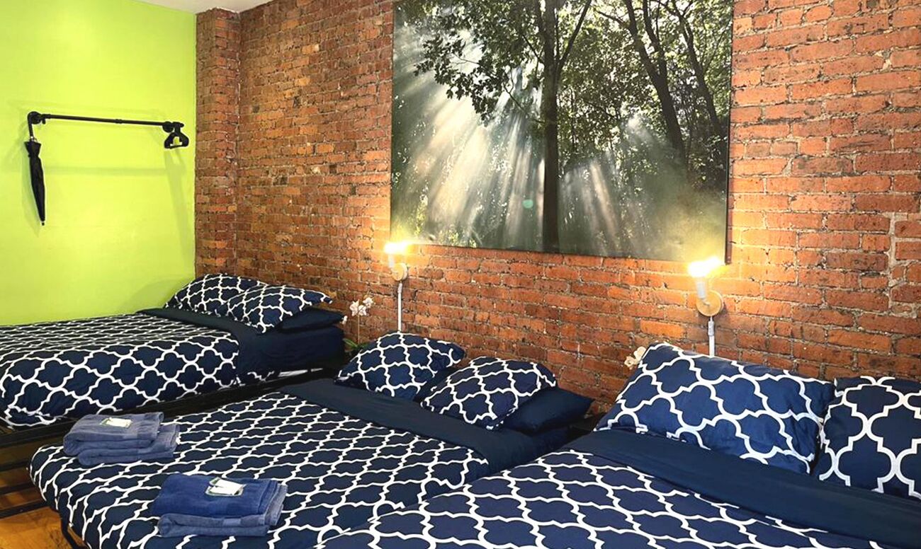 A room with two beds, each with matching patterned bedding, a brick wall, and a large window with a forest view.