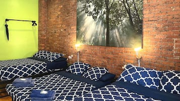 Een kamer met twee bedden, elk voorzien van beddengoed met hetzelfde patroon, een bakstenen muur en een groot raam met uitzicht op een bos.