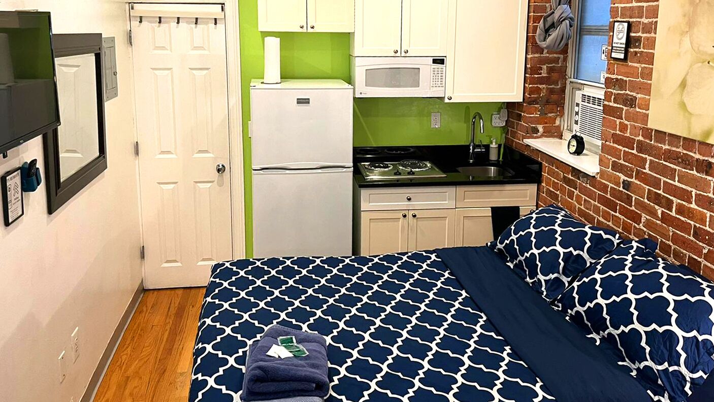 Una stanza compatta con un letto, un angolo cottura, un frigorifero e un forno a microonde.