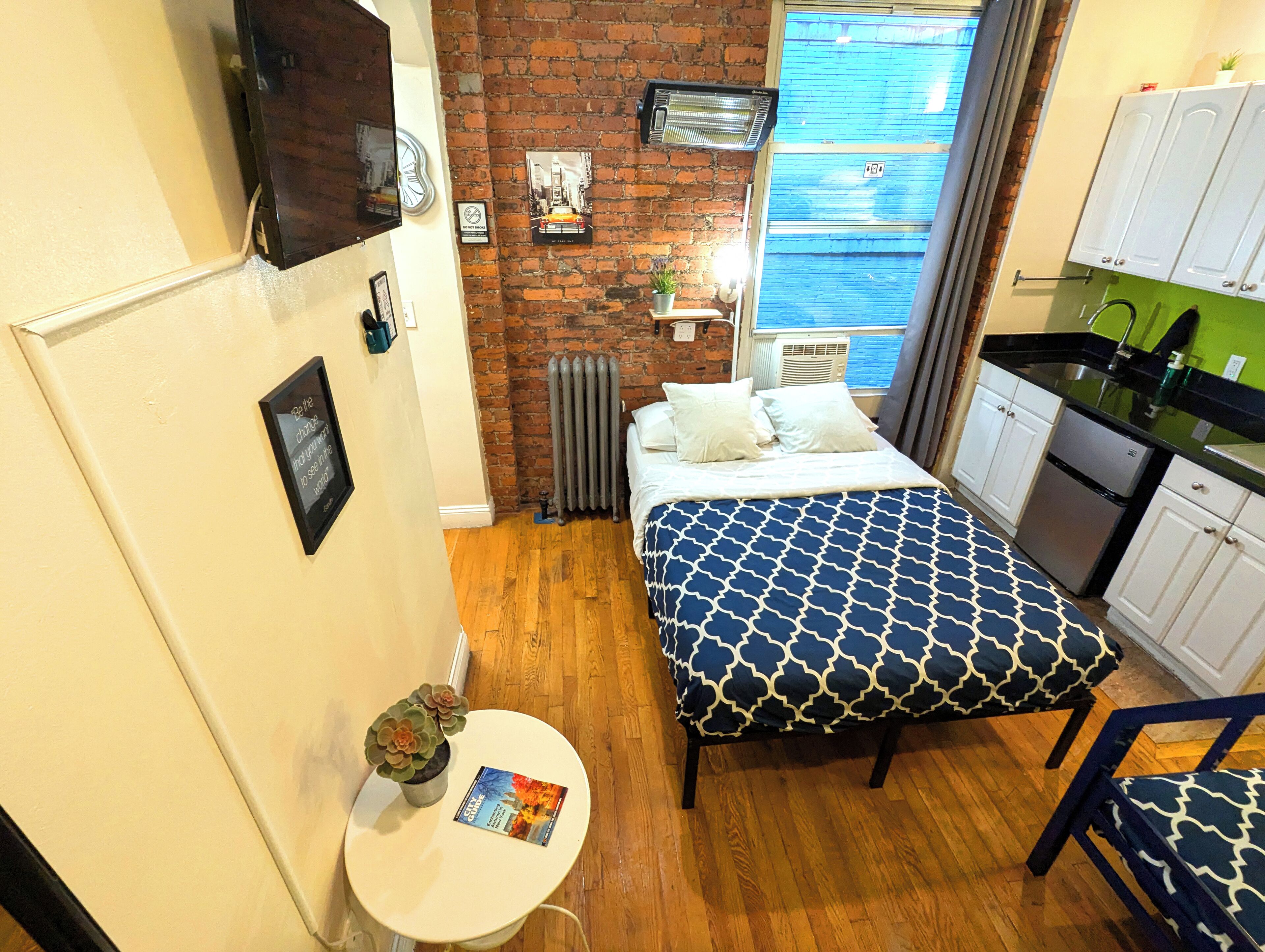Une petite chambre comprenant un lit, une petite table avec une plante, un radiateur et une fenêtre donnant sur la mer.