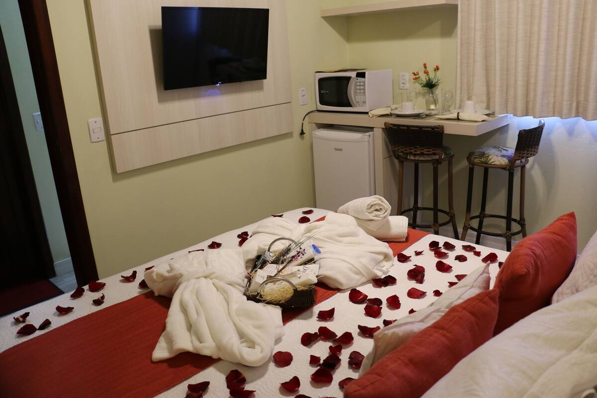 Quarto de hotel com cama, televisão, micro-ondas, frigorífico e um pequeno bar com bancos.