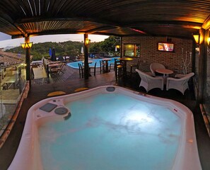 Un jacuzzi con vista a la piscina, mobiliario exterior y una pantalla de televisión.