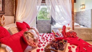 Un décor romantique avec un lit, des pétales de rose, un bouquet de fleurs et une bouteille de champagne.