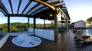 Une terrasse en bois avec un jacuzzi, un coin salon extérieur et une vue sur le paysage.