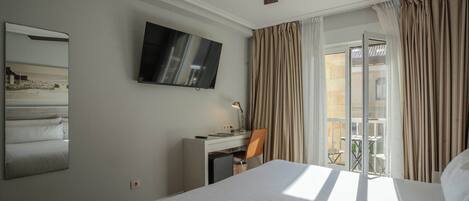 A hotel room with a bed, a desk, a chair, a TV, and a balcony with curtains.
