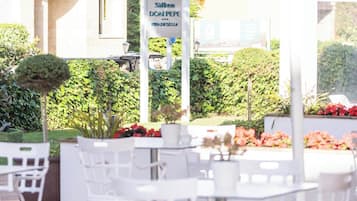 An outdoor patio with white chairs and tables, a sign for 'Silken DON PEPE PIADE SESSA,' and a building in the background.