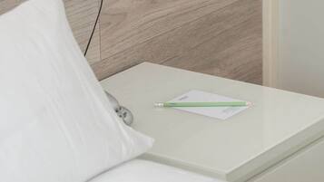 A neatly made bed with a white pillow and a green pen on a white bedside table.