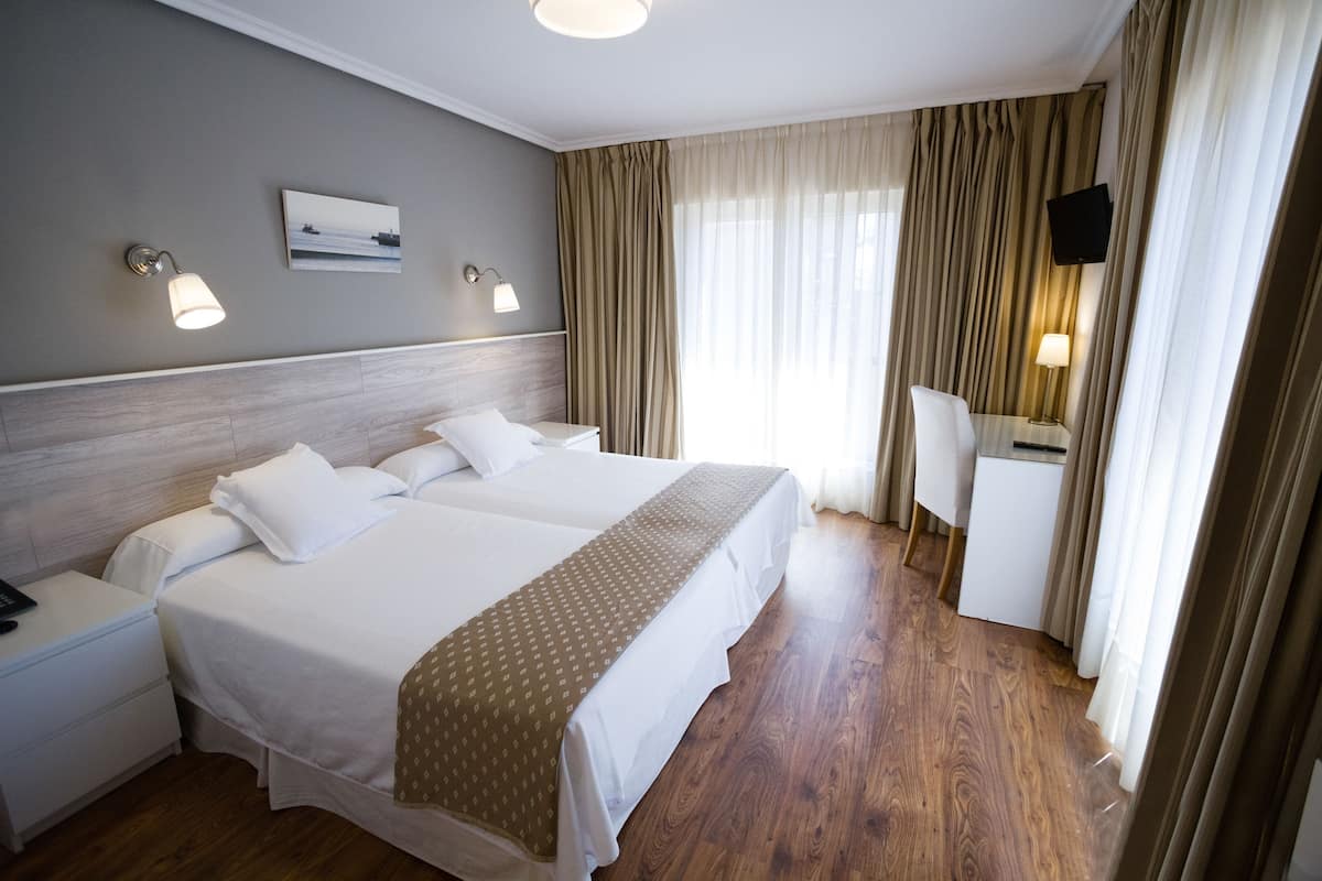 Ein Hotelzimmer mit zwei Betten, einem Schreibtisch, einem Stuhl, einem Flachbildfernseher und einem Bild an der Wand.