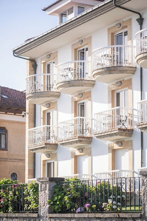 A multi-story building with balconies, a stone base, and a metal fence.