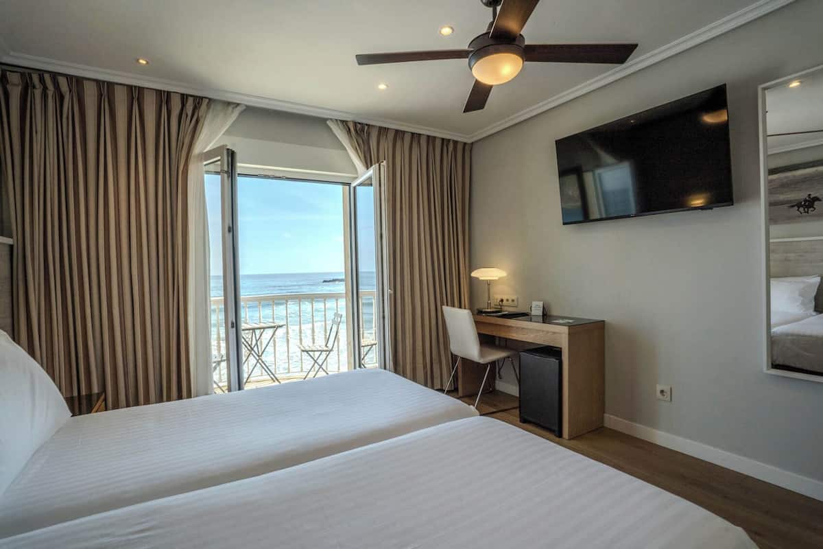 Ein Hotelzimmer mit Bett, Schreibtisch, Stuhl, Fernseher und einem Balkon mit Meerblick.