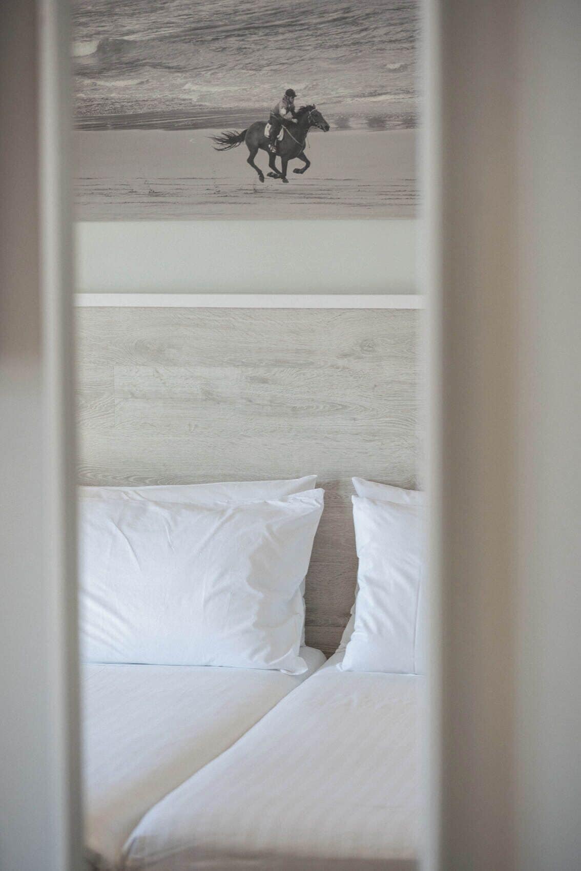 A bed with white linens and a painting of a horse rider on the wall above.