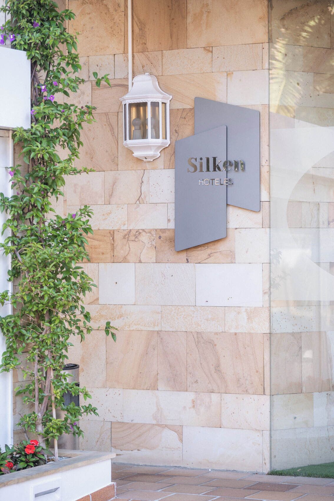 A hotel entrance with a stone wall, a sign reading 'Silken Hotels,' and a white lantern.