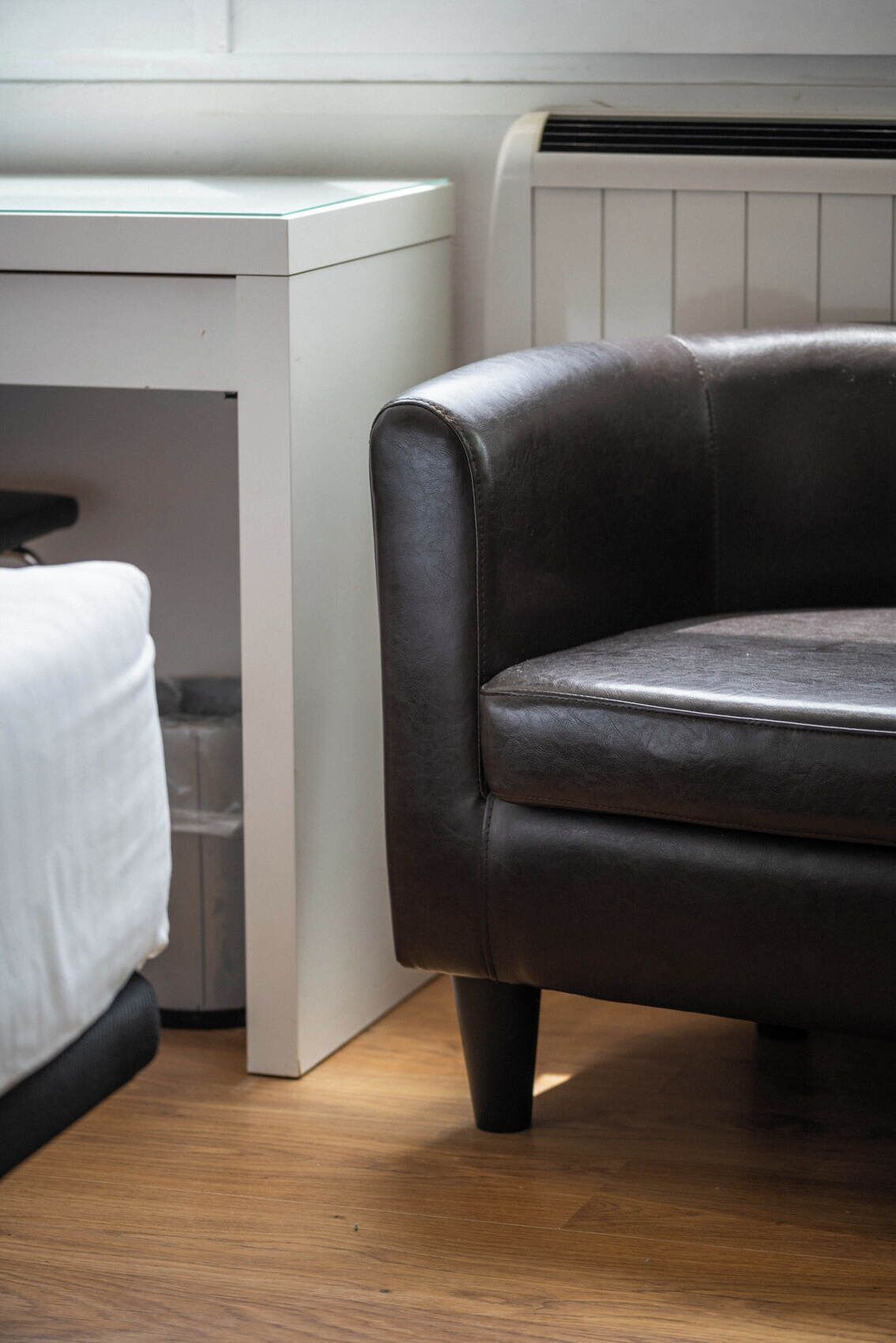 Una habitación con un sofá de cuero oscuro, un escritorio blanco y un radiador.