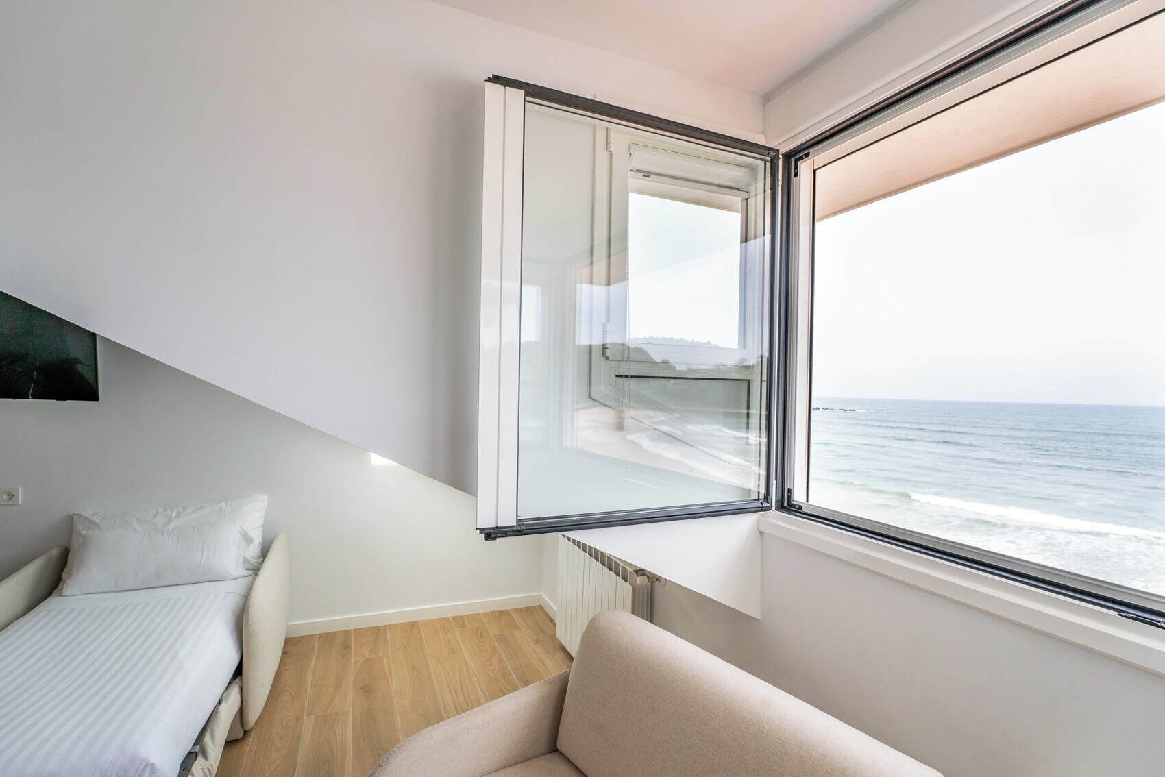 A bedroom with a large window, a bed, a sofa, and a view of the sea.