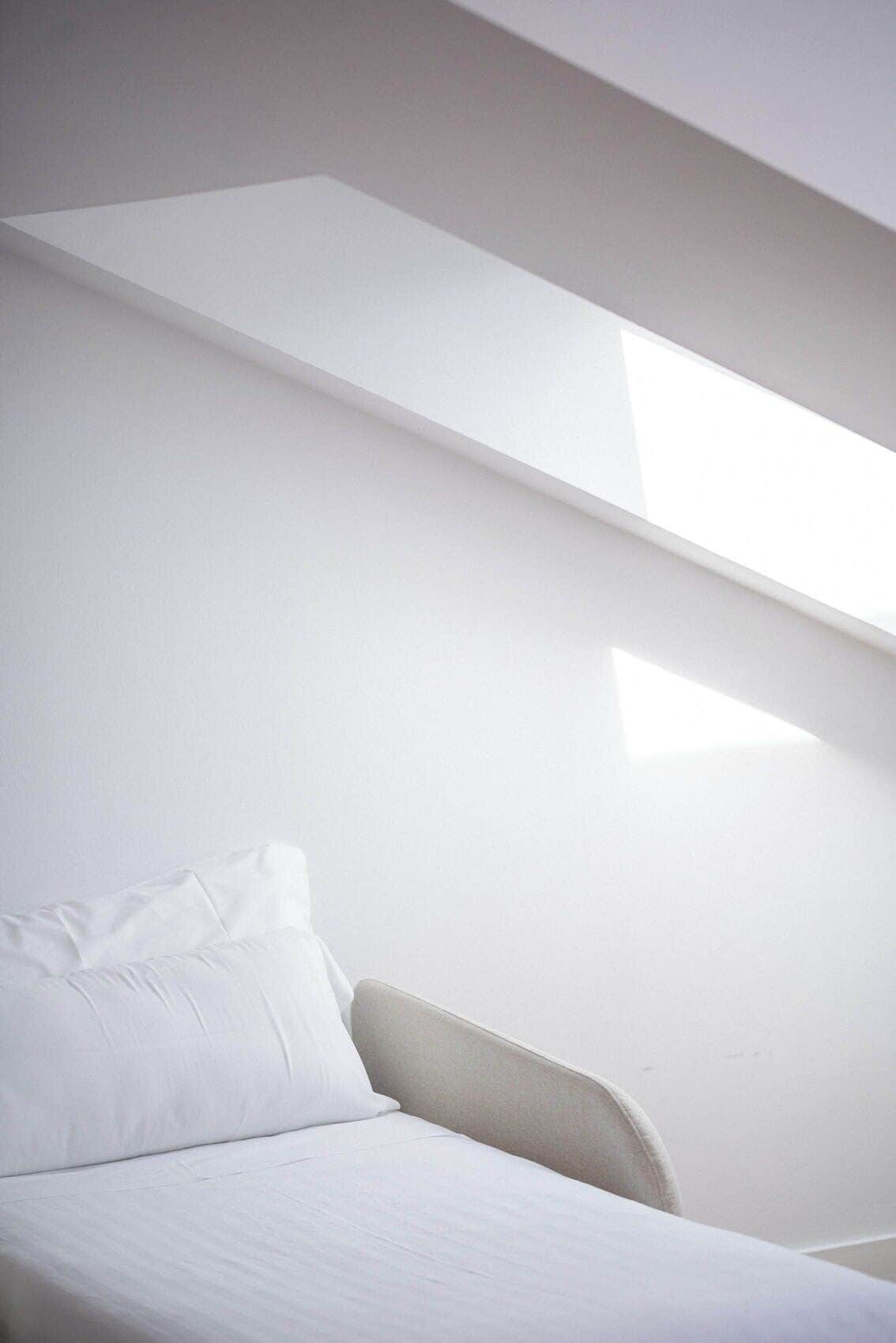 Ein schlicht eingerichteter Raum mit einem Bett, einem Sessel und einer schrägen Decke.