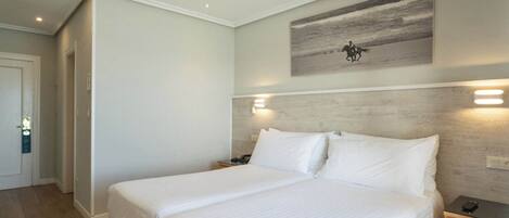 Una habitación de hotel con una cama grande, mesitas de noche, un cuadro en la pared y una puerta que da a otra habitación.