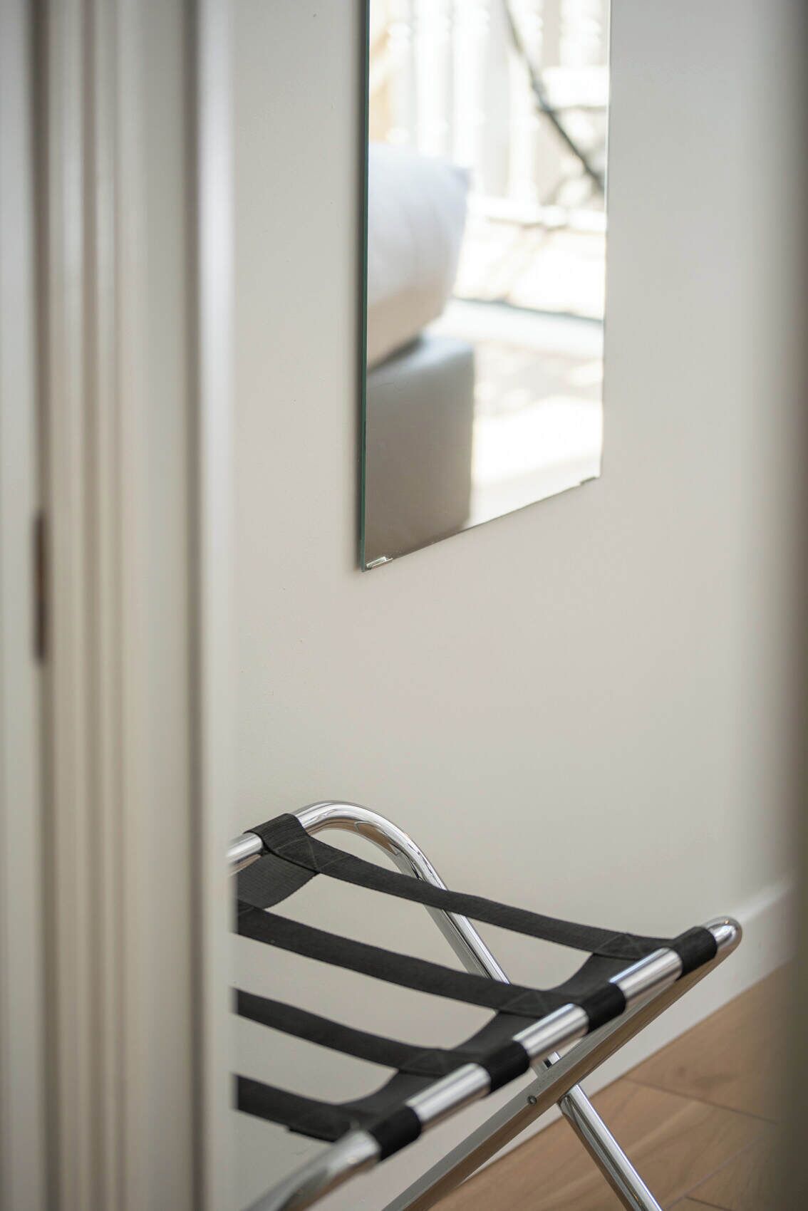 Een kamer met een stoel met metalen frame, een spiegel aan de muur en een raam met uitzicht op de omgeving.