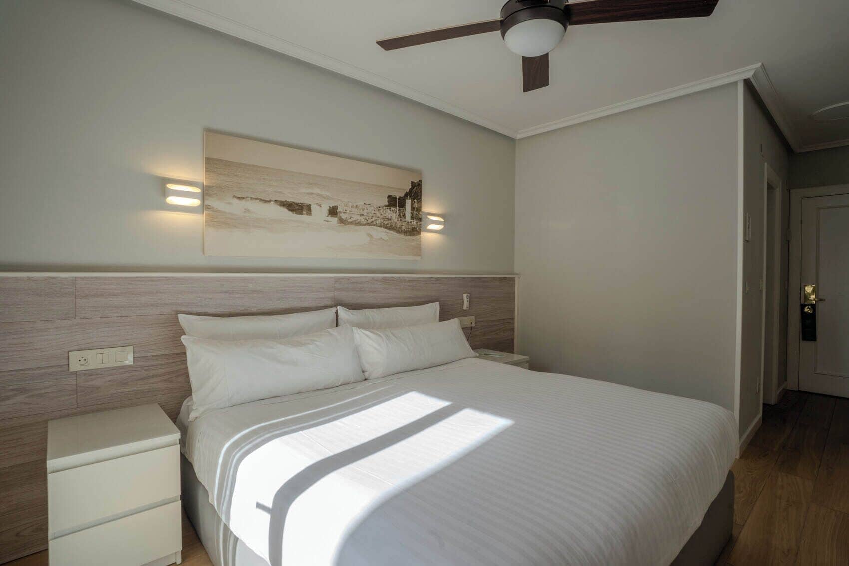 A bedroom with a bed, bedside tables, a ceiling fan, and a wall-mounted light fixture.