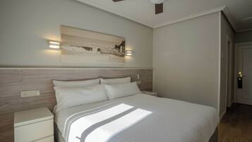 A bedroom with a bed, bedside tables, a ceiling fan, and a wall-mounted light fixture.
