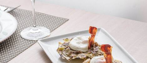 A dining table with a white plate of food, a glass of red wine, and a woven placemat.