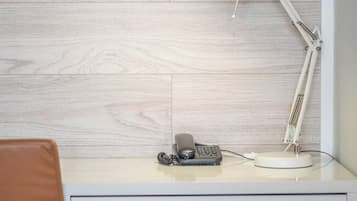 Escritorio con lámpara, teléfono y un pequeño dispositivo negro, posiblemente una impresora, frente a una pared de madera.