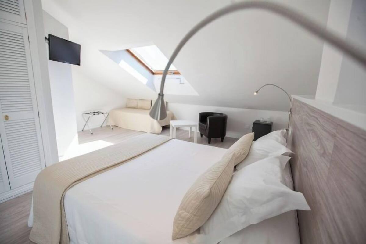 Ein modernes Schlafzimmer mit einem großen Bett, einem Schreibtisch, einem Sessel und einem an der Wand befestigten Fernseher.