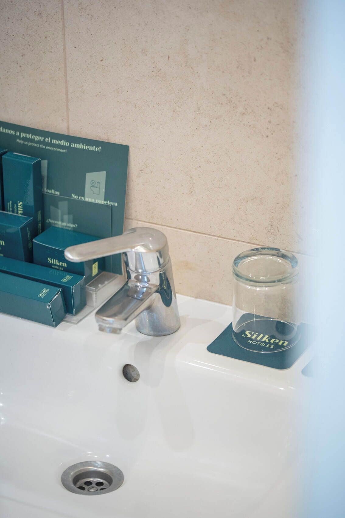 Un lavandino con un rubinetto, un vasetto di vetro e scatole con la scritta 'Silken Hotels'.