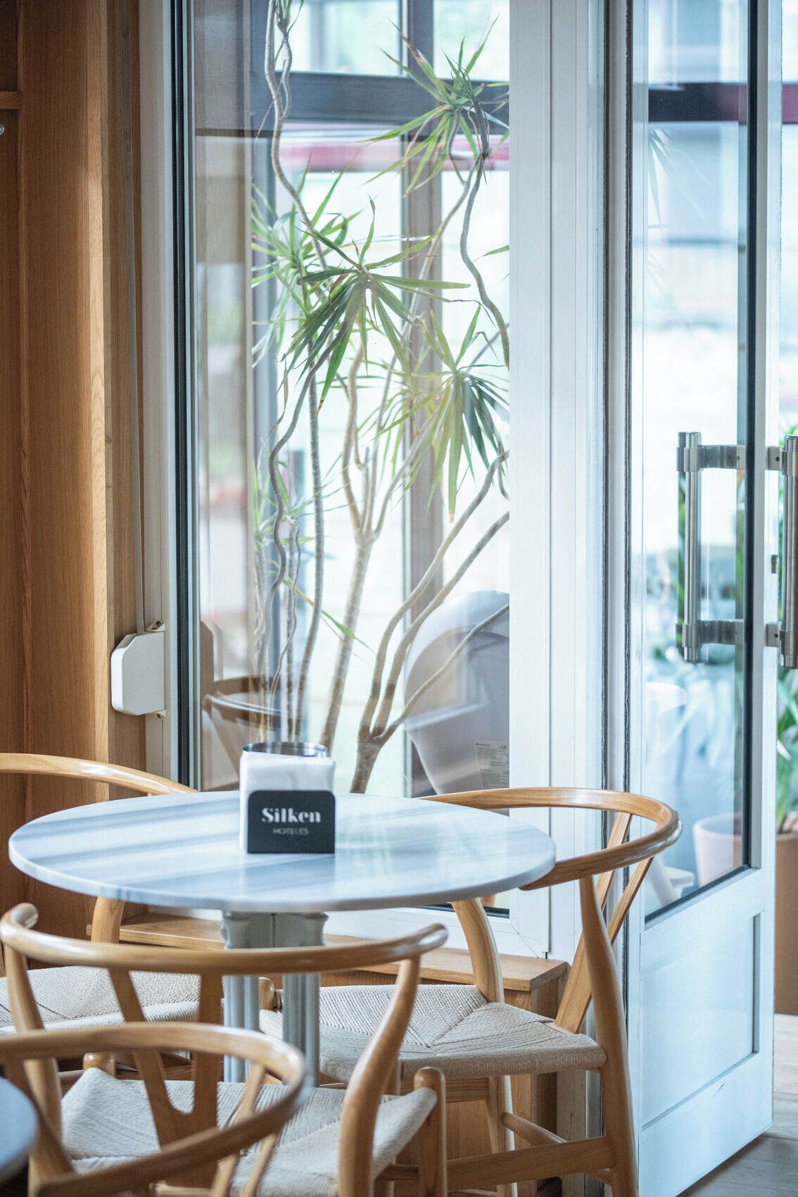 Et rundt bord med stole, en potteplante og et skilt med teksten 'Silken Hotels'.