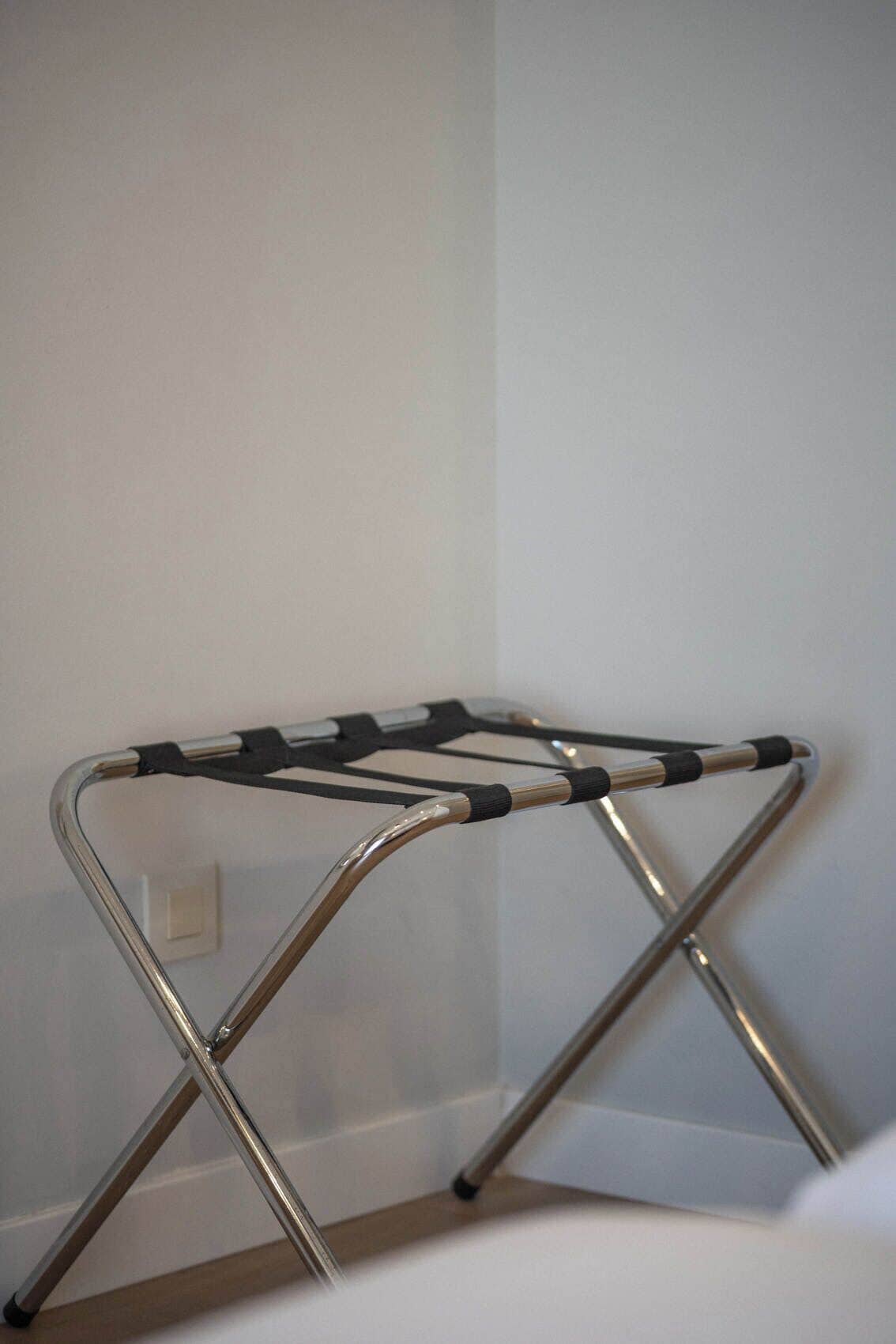 A metal folding chair with a black seat and backrest, positioned against a white wall.