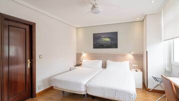 Habitación de hotel con dos camas, una puerta de madera, un ventilador de techo, un cuadro en la pared y una ventana.