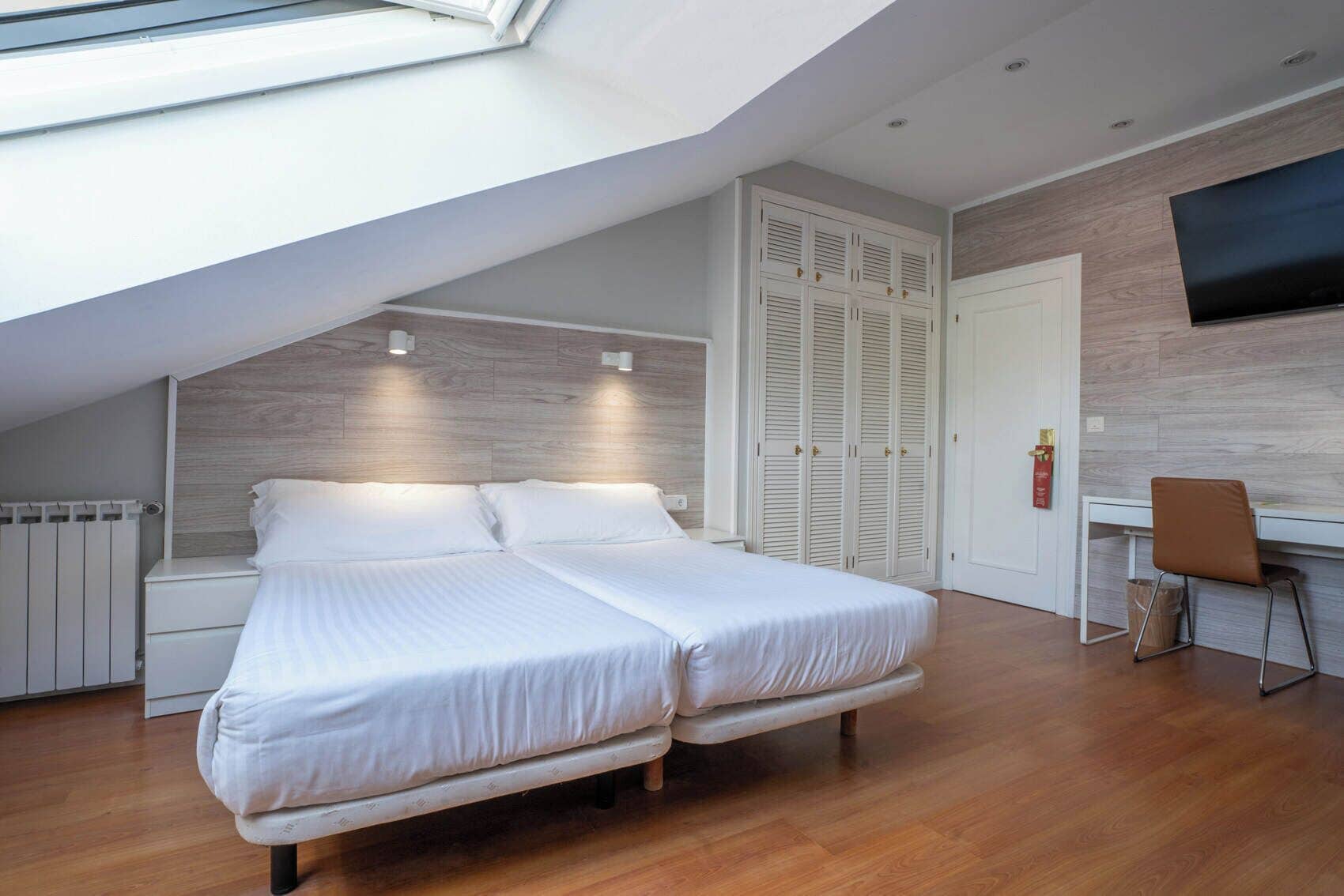 Une chambre avec deux lits, un bureau, une chaise, une armoire et un téléviseur fixé au mur.