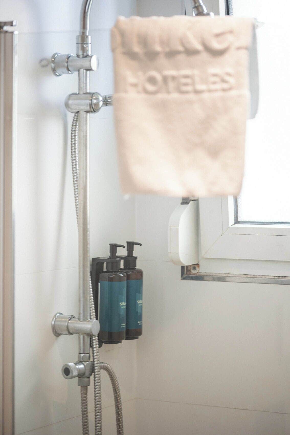 A shower with a towel hanging, a window, and two bottles of shampoo.