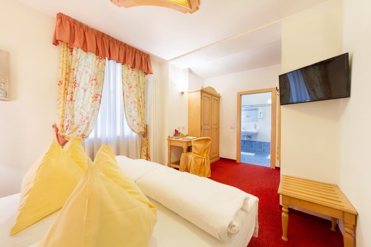 A hotel room with a bed, a desk, a wardrobe, a television, and a red carpet.