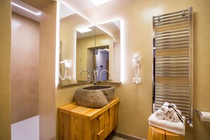 Un baño con lavamanos de piedra, tocador de madera, un espejo, toallero y secamanos.