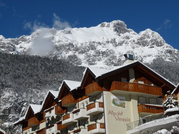Un hotel con varios balcones, montañas nevadas al fondo y un cartel que dice